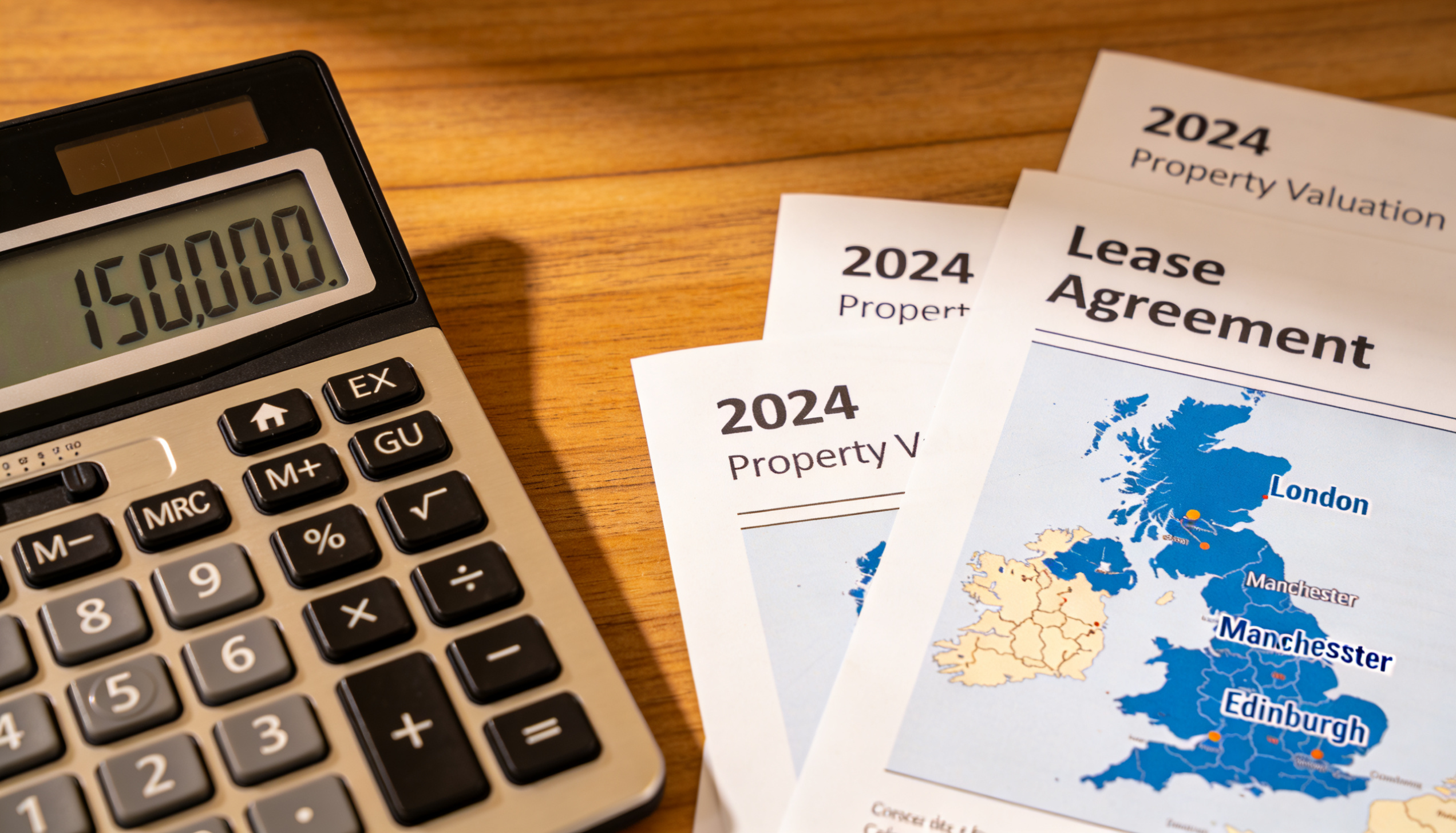 A calculator, property documents, and a UK map on a wooden desk.