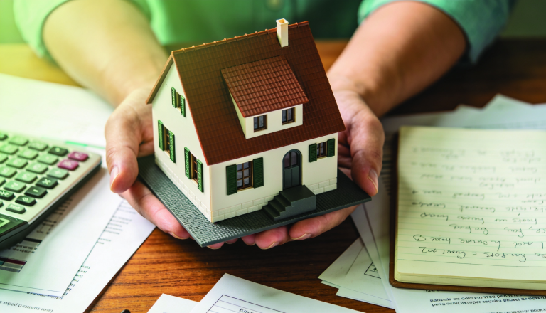 A person examining a small property model with a calculator and notepad, symbolizing budget-friendly investment strategies.
